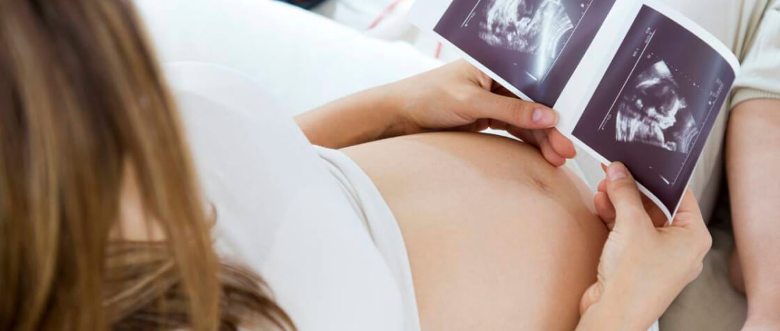 A pregnant woman is looking ultrasound picture of her baby.
