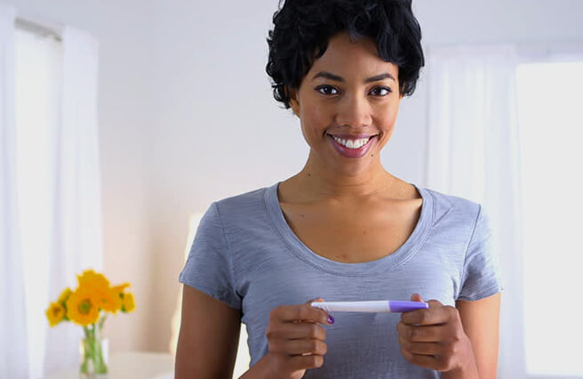 A black woman is holding a pregnancy test.