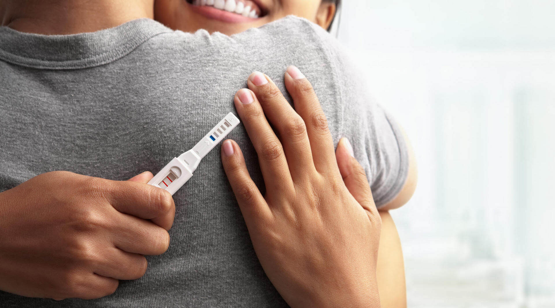 happy couple hugging while lady holds positive pregnancy test